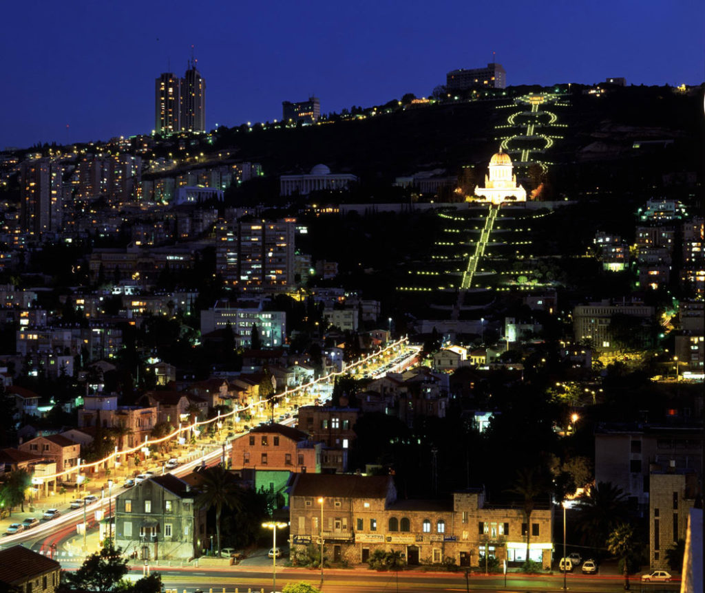 Haifa esti kivilágításban: a hegy lábánál a Német Templomosok piros cserepes házai, fentebb a bahá’í kert © Bahá’í Nemzetközi Közösség media.bahai.org